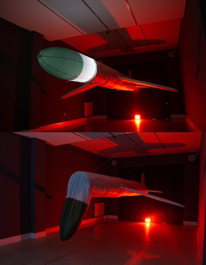 A missile model hangs in a room lit red.