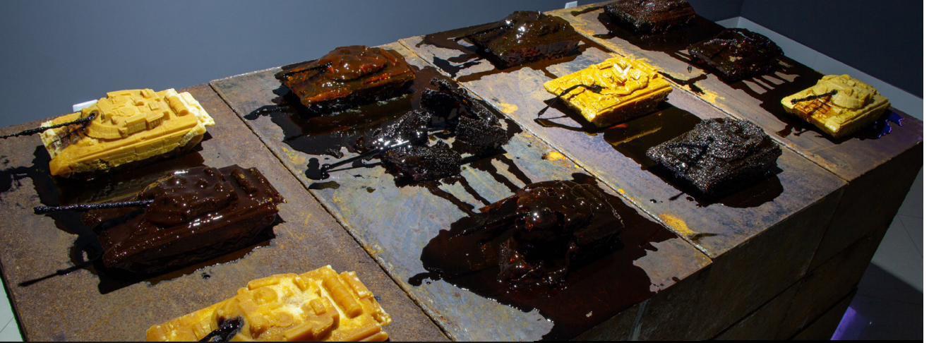 Small tanks made of sugar, some melted into dark syrup, on steel plates.