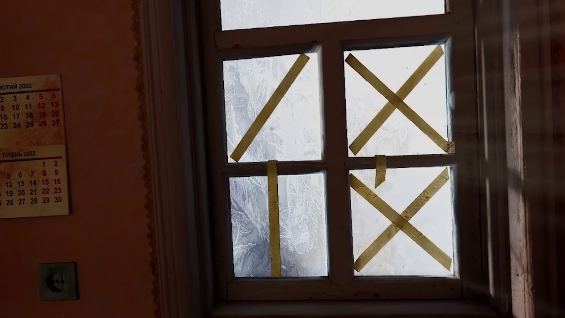 A window taped with crossed paper strips; snow outside.